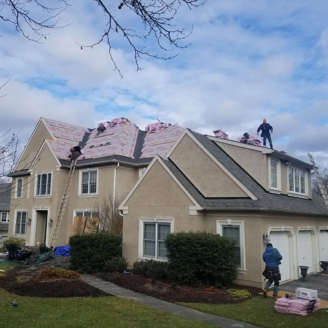 Workers installing roof shingles on house.