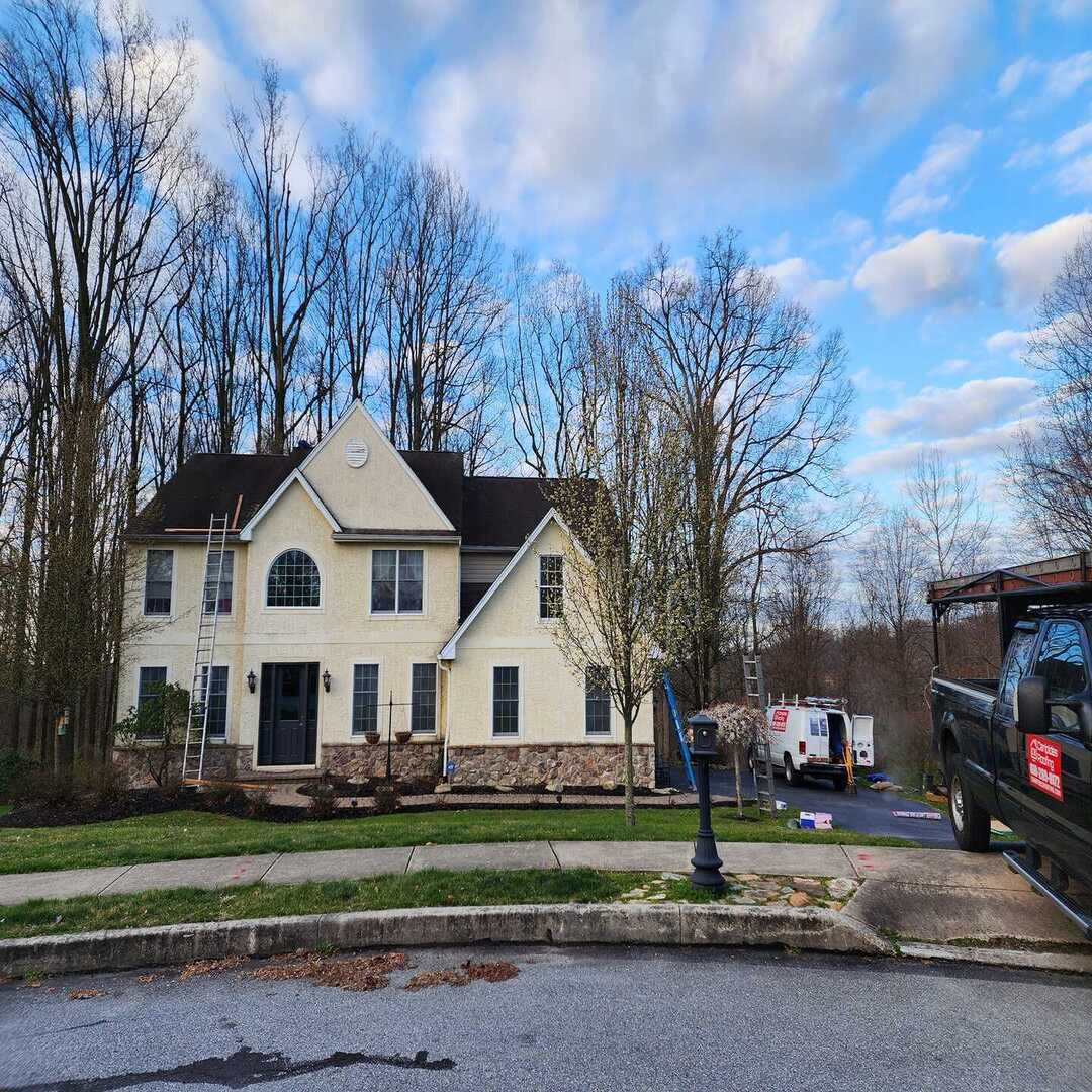 Two-story house with ladders, vehicles nearby.