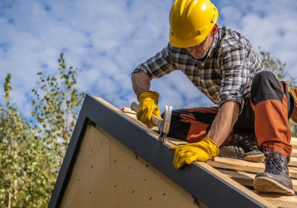 Roofer hammering on house roof construction.